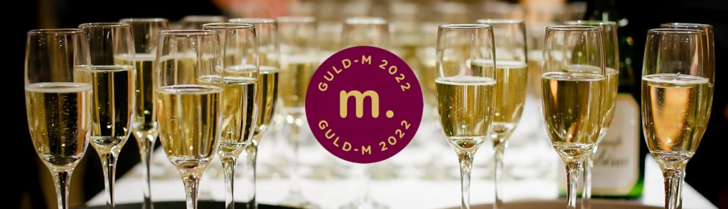 Guld M emblem mot champagneflaskor